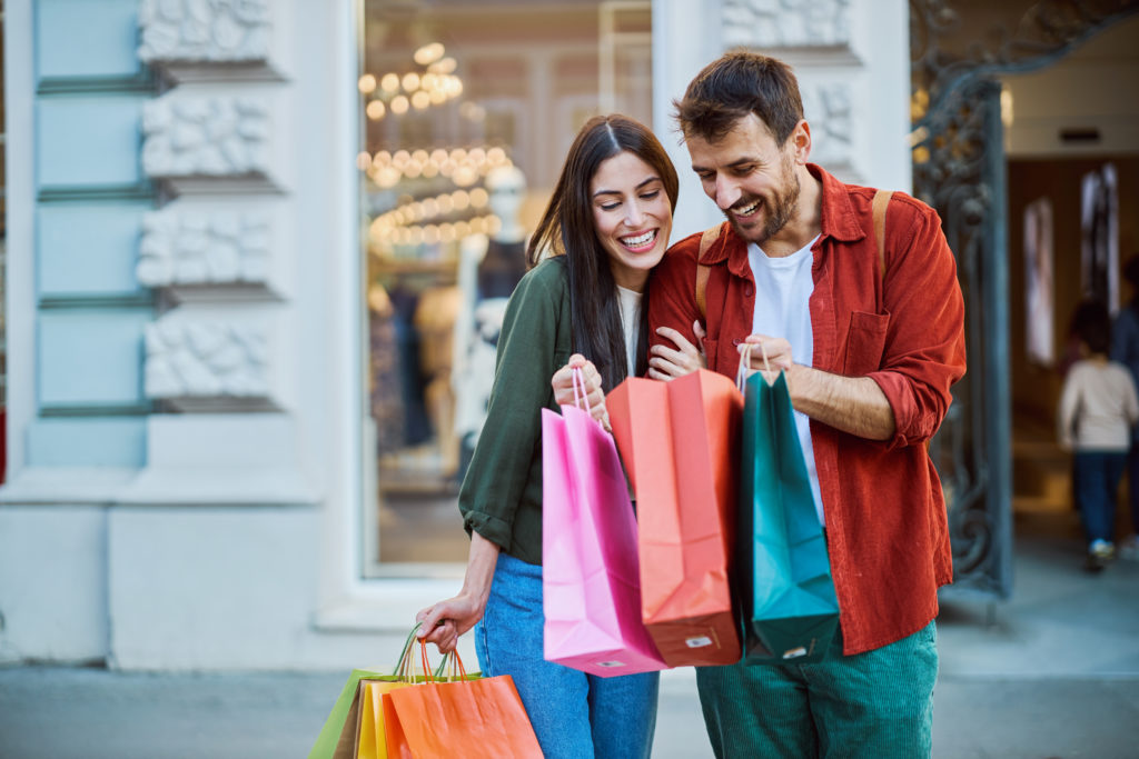Happy couple looking at shopping bags in front of a store window